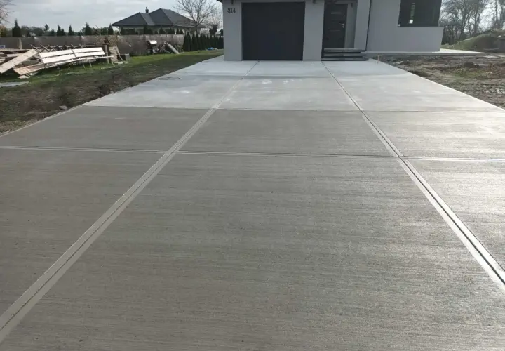 Nowy podjazd z beton stemplowany, z wyraźnymi fugami, prowadzi do nowoczesnego domu z szarą bramą garażową.