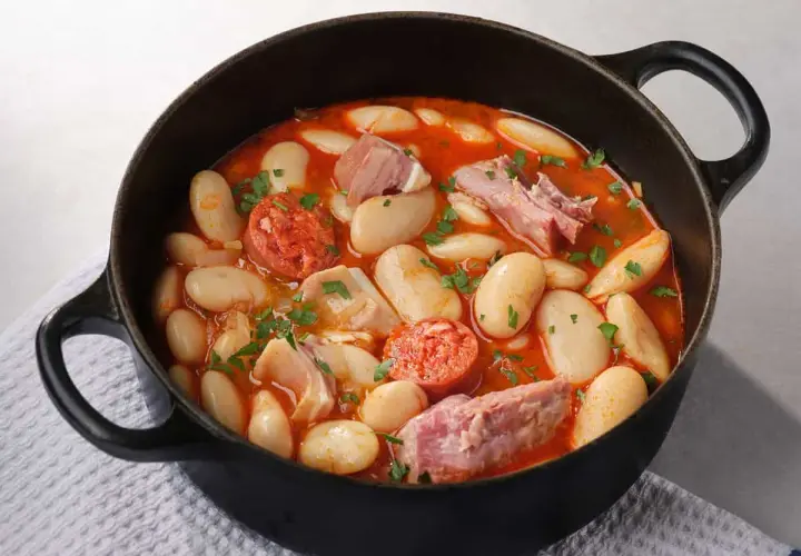 Judiones de la granja en cazuela negra, con chorizo, tocino y perejil picado. Un plato reconfortante y lleno de sabor.