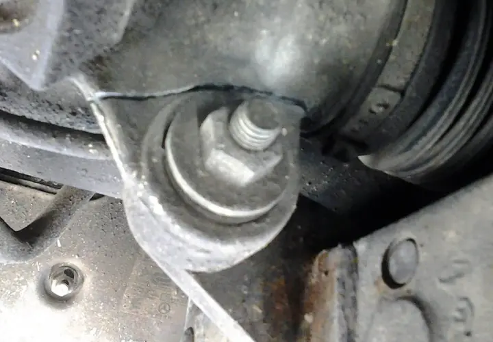 Soporte metálico con un perno hexagonal sujetando una pieza del motor, cerca de un componente que podría ser parte del volante de dirección.