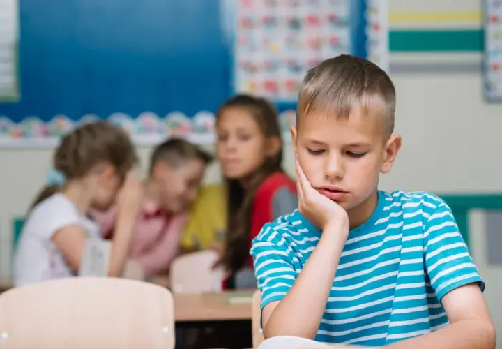 Un bambino solo in classe, con la mano sul viso, mentre altri bambini ridono e parlano tra loro. Sembra che mia figlia non abbia amici.