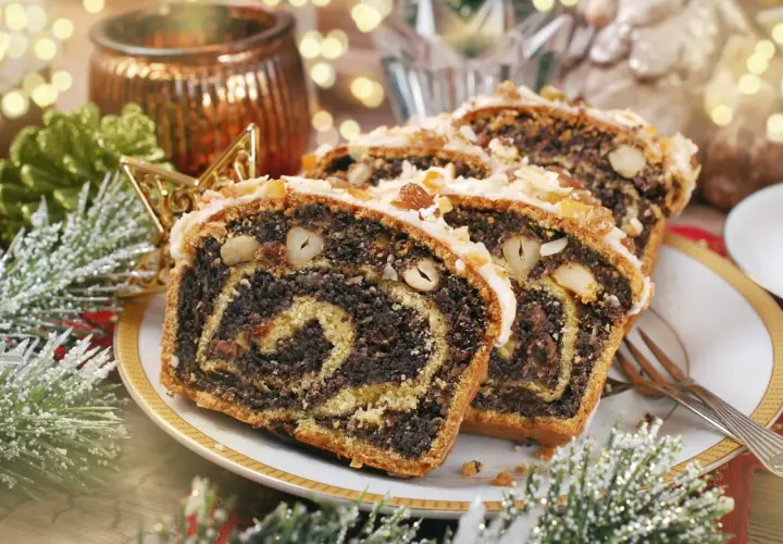 Stary przepis na makowiec, bogato nadziany makiem i bakaliami, ozdobiony lukrem i orzechami, na tle świątecznych dekoracji.