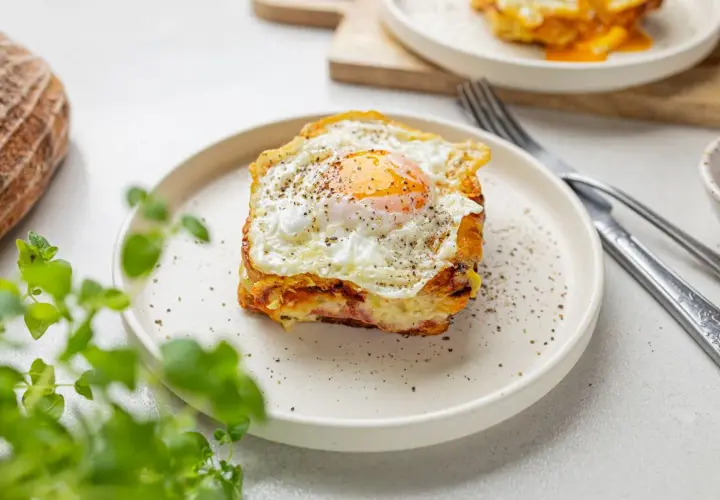 Pyszny croque madame z jajkiem sadzonym na wierzchu, podany na talerzu z pieprzem.