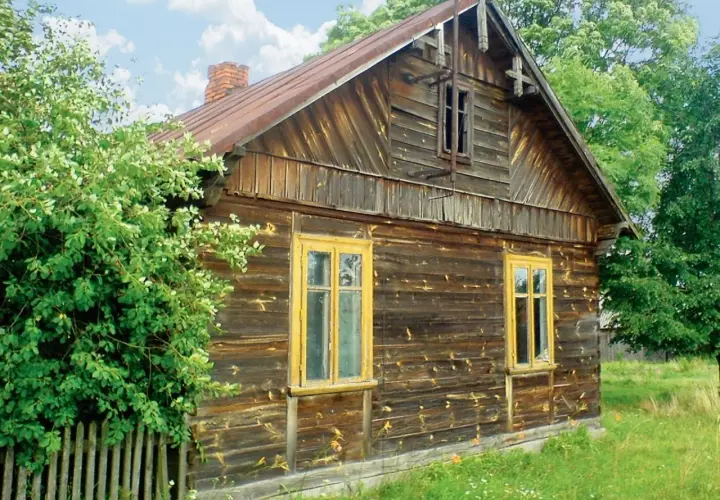 Stary, drewniany dom z żółtymi oknami, otoczony zielenią. Wnętrze tego domu kryje zapewne wiele historii.