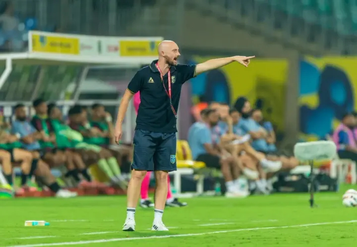 Tomasz Tchórz, trener, wskazuje kierunek na boisku. Za nim siedzą zawodnicy na ławce rezerwowych.