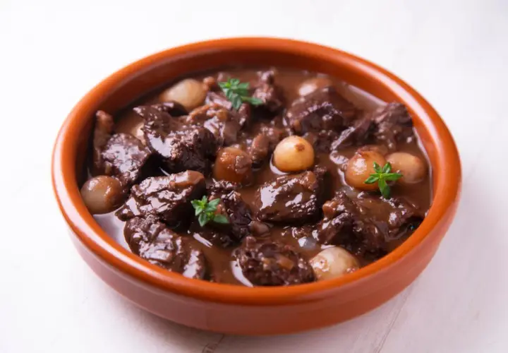 Herzhaftes Spezzatino di manzo mit kleinen Zwiebeln und Kräutern in einer Terrakotta-Schale.