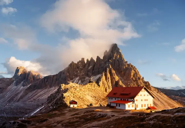 Sonnenuntergang an einer Berghütte. Die schroffen Gipfel der Dolomiten ragen hinter dem Gebäude auf. Hier könnte man gut zwei Wochen auf der Alm arbeiten.