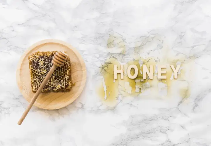 Plaster miodu z drewnianym mieszadełkiem na talerzyku i napis "HONEY" z miodu na marmurowym tle.