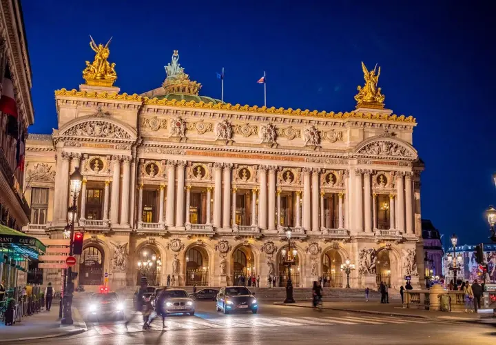 Słynny teatr w Paryżu, Opera Garnier, lśni w nocnym świetle. Złote rzeźby i bogata fasada zapraszają na wieczór pełen wrażeń.