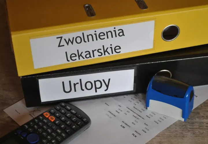 Segregator "Zwolnienia lekarskie" i "Urlopy" obok kalkulatora i pieczątki. Dokumenty gotowe do archiwizacji, może to być kod c na l4.