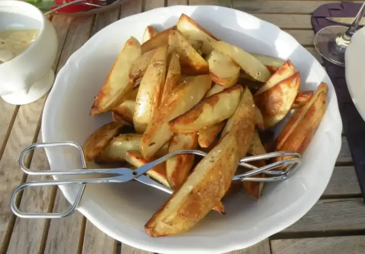 En skål med gyllene klyftpotatis i ugn, redo att serveras med en sallad och dipp.