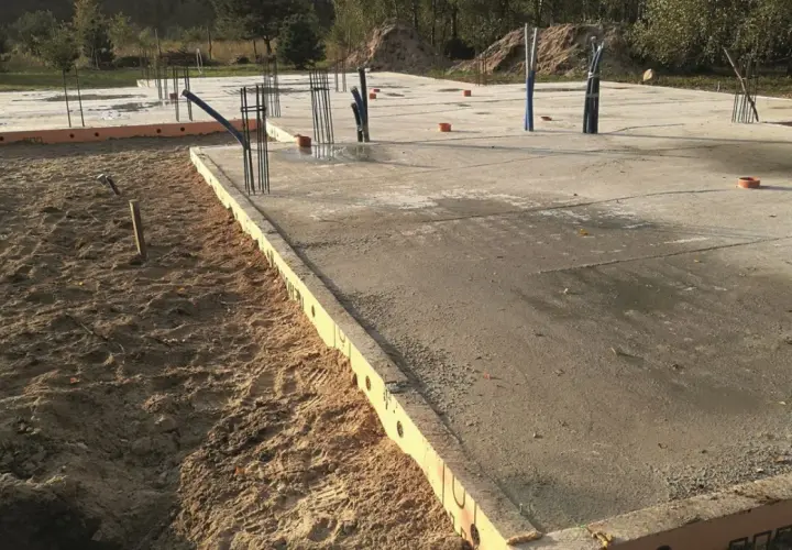 Szalunek płyty fundamentowej z widocznymi zbrojeniami i instalacjami. Betonowa płyta fundamentowa w trakcie budowy.