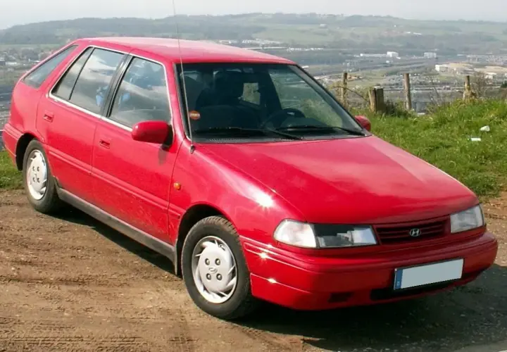 Czerwony Hyundai Pony stoi na polnej drodze, z widokiem na krajobraz w tle.