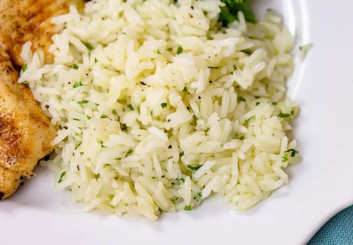 Fluffy white rice with flecks of green herbs, perfect for a simple rice seasoning recipe. A side of grilled chicken is visible.