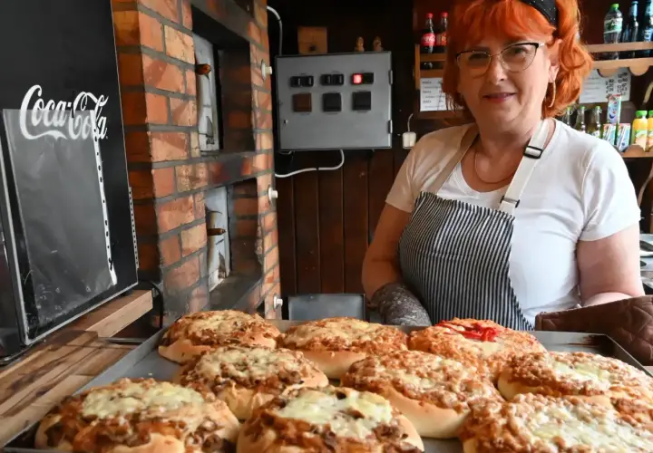 Kobieta z rudymi włosami prezentuje świeżo upieczone pizze w najstarszej pizzerii w Polsce. W tle widać ceglany piec i tablicę z logo Coca-Coli.