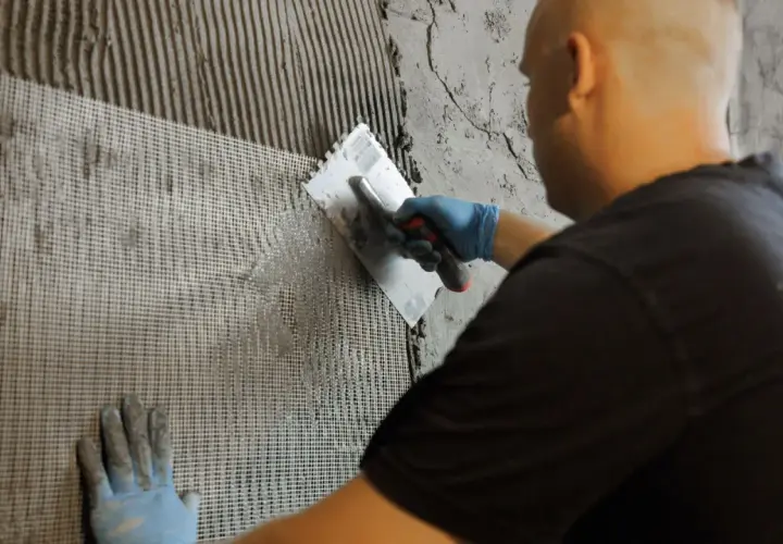 Hand mit blauer Handschuh trägt Mörtel auf ein Gitter auf der wu wand auf.