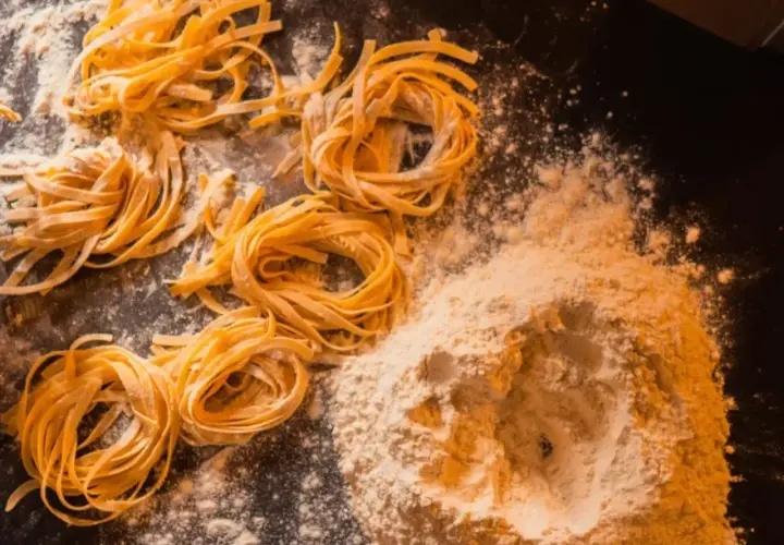 Domowy makaron, jak u babci! Świeże tagliatelle uformowane w gniazda, obok kopczyka mąki. Przepis babci na pyszne danie.
