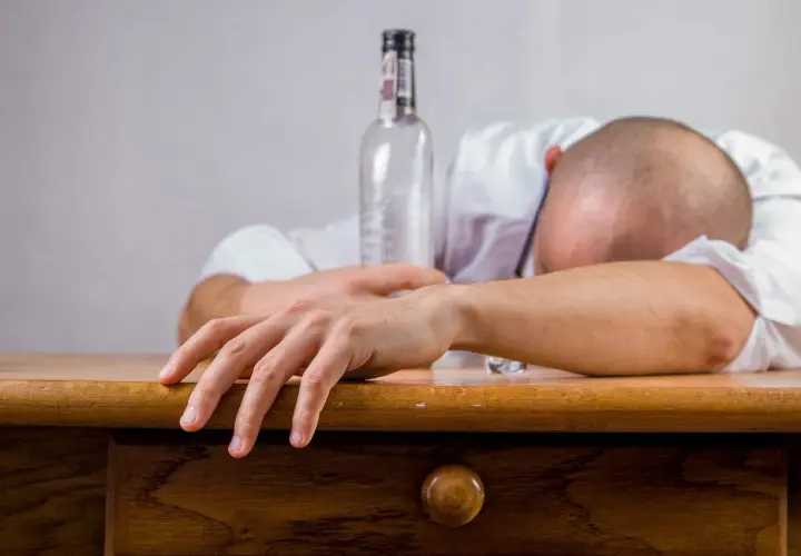 Mężczyzna śpi na biurku obok pustej butelki. Czy alkohol wypłukuje żelazo? To pytanie zadaje sobie wielu.