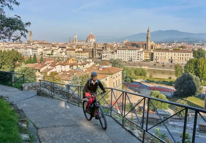A woman enjoys an Italy bike tour, cycling with Florence's iconic skyline behind her.
