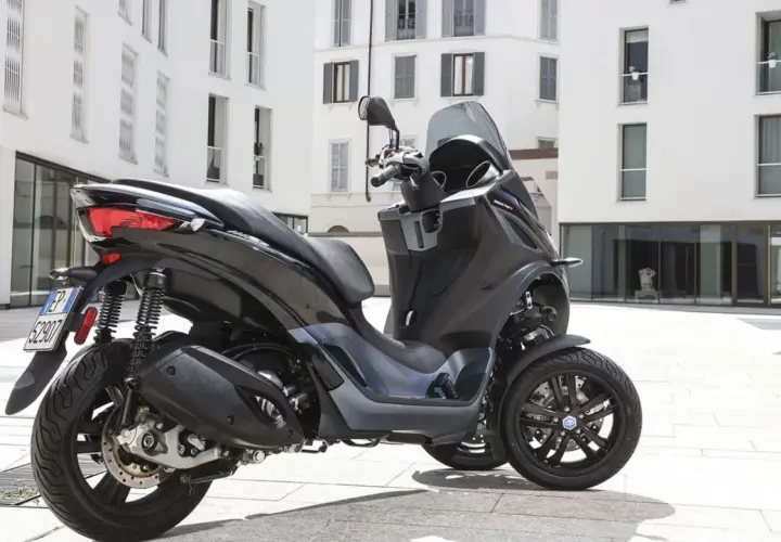 Un Piaggio MP3 300 negro aparcado en una plaza urbana. Su diseño de tres ruedas ofrece estabilidad y un consumo eficiente.