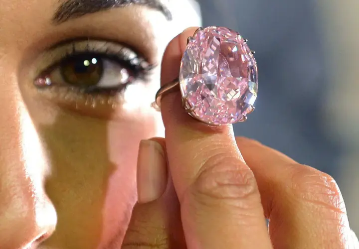 Ein riesiger, pinker Diamantring wird von einer Hand gehalten. Man fragt sich, wie viel kostet ein Kilo Diamant?