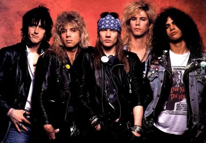 Guns N' Roses członkowie w skórzanych kurtkach i z charakterystycznymi fryzurami. Axl Rose w bandanie, Slash z burzą loków.