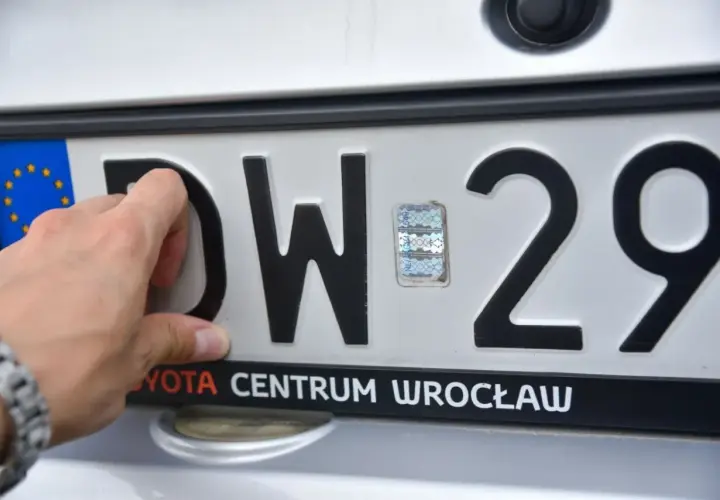 Dłoń przykłada tablicę rejestracyjną na bagażnik rowerowy. Widoczne litery DW i cyfry 29.