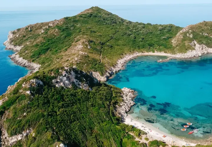 Idealna pogoda na Korfu we wrześniu: turkusowa zatoka, zielone wzgórza i piaszczysta plaża z łódkami.