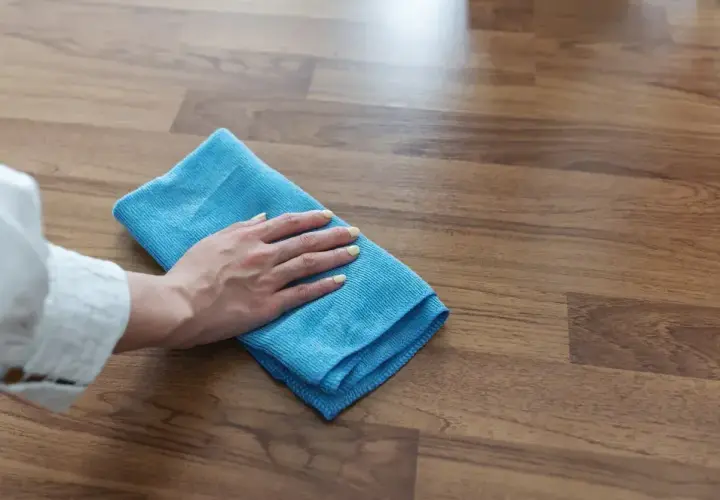 Mano con panno blu pulisce pavimento in gres effetto legno. Scopri come togliere la colla dal pavimento in gres con metodi efficaci.