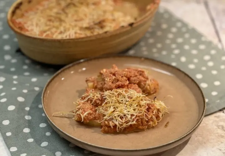 Dos porciones de gnocchi alla romana gratinados con queso, servidos en un plato marrón sobre un mantel de lunares.