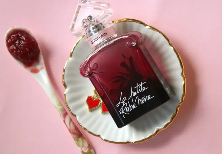 Elegancka buteleczka perfum Guerlain La petite robe noire z uroczymi serduszkami, obok łyżeczka z dżemem.