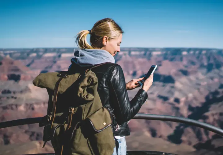 Kobieta z plecakiem w Wielkim Kanionie sprawdza telefon, planując dalszą podróż – roaming krajowy a międzynarodowy.