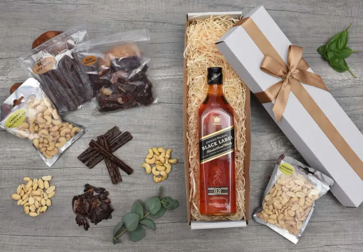 Jak przygotować prezentowy zestaw whisky dla początkującego konesera: butelka Johnnie Walker Black Label, suszone mięso, orzechy i eleganckie pudełko.