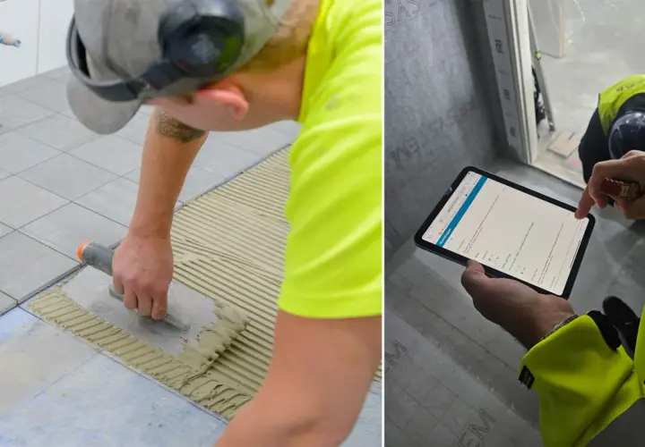 Byggare lägger klinker på ett badrumsgolv. En annan person kontrollerar arbetet på en surfplatta.