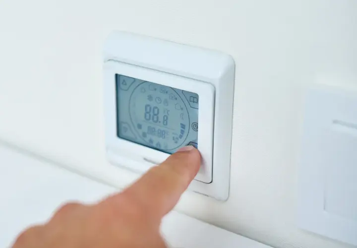 Palec naciska przycisk termostatu, ustawiając idealną temperaturę pieca gazowego.