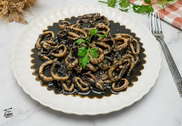 Plato de calamares en su tinta, con anillas tiernas y sabrosas, decorado con perejil fresco. Un clásico irresistible.