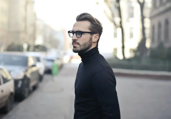 Elegancki mężczyzna w okularach i czarnym golfie, zamyślony, jakby planował zagrywki zakochanego faceta.