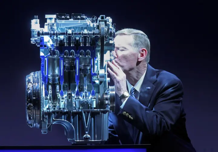 Mężczyzna w garniturze całuje silnik Forda. Wiele osób szuka **1.0 ecoboost opinie** przed zakupem.