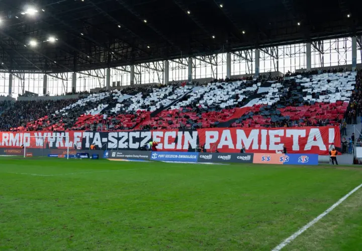 Trybuna stadionu podczas meczu Pogoń Szczecin – Widzew Łódź. Kibice tworzą biało-czerwony transparent "ARMIO WYKLETA-SZCZECIN PAMIĘTA!".