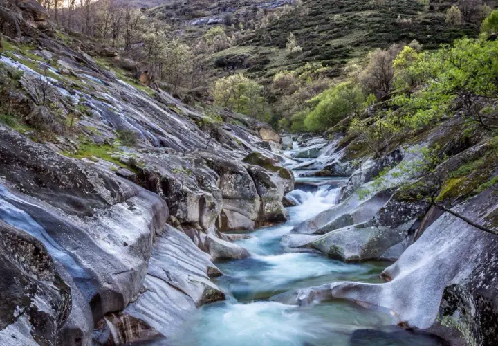 El **camino del agua** serpentea entre rocas erosionadas y vegetación verde, creando un paisaje natural sereno.