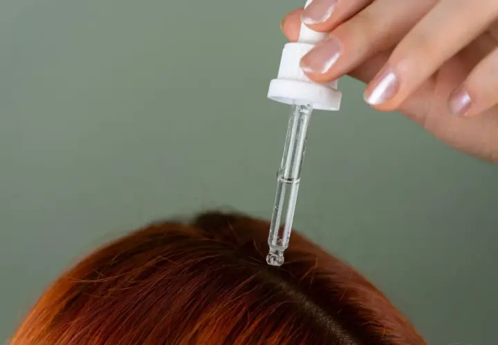 Kropla serum z pipety spada na rudą skórę głowy. To może być początek pielęgnacji z cerkogelem.