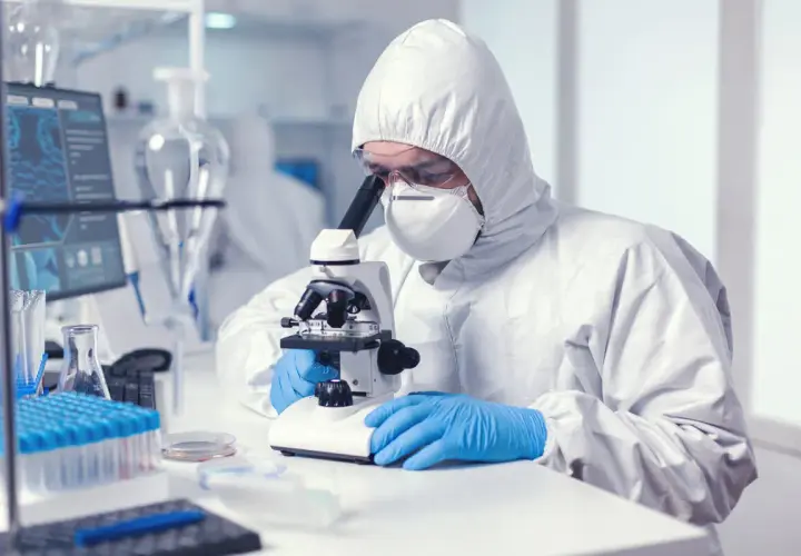 Analityk medyczny w kombinezonie ochronnym bada próbki pod mikroskopem w laboratorium.
