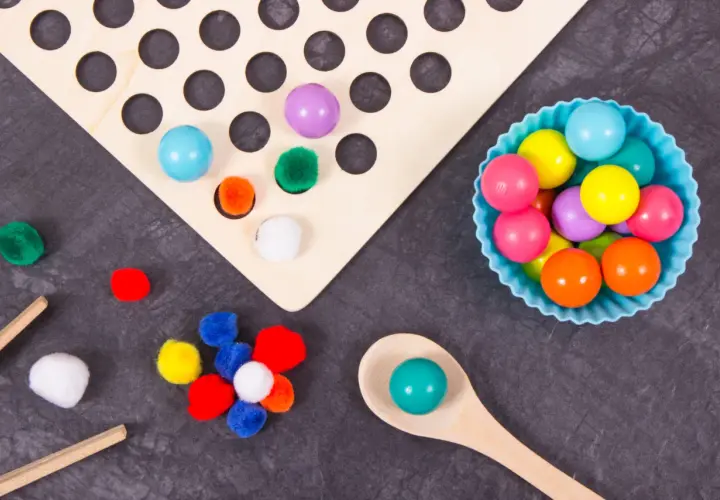 Juego heuristico materiales: pompones, bolas de colores y cuchara de madera para explorar texturas y formas.