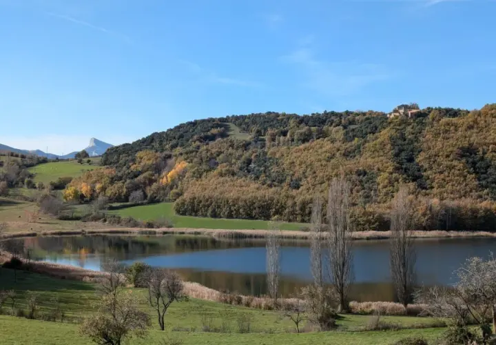 El estany de Montcortès, un espejo de agua sereno rodeado de colinas otoñales y un cielo azul claro.
