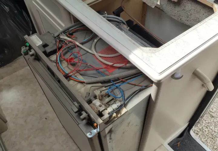 Réparation du frigo camping-car 12v 220v gaz Dometic en panne. Câblage apparent et composants exposés.