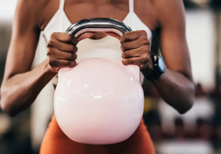 Kobieta z rozbudowanymi ramionami trzyma różową kettlebell, ćwicząc, by badz sprawny jak lampart.