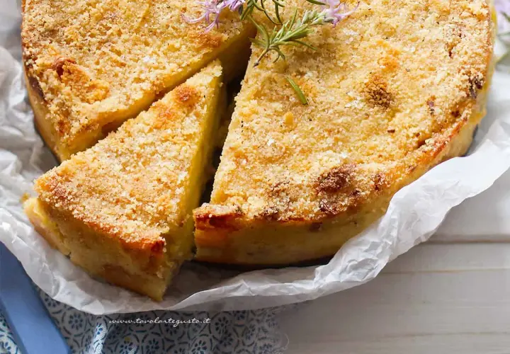 Delizioso gateau di patate dorato e croccante, guarnito con rosmarino fresco. Una fetta è già stata tagliata, invitando ad assaporare questo piatto.