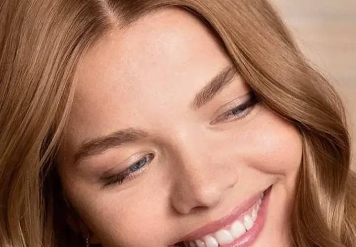 Sonrisa radiante de una mujer con marron ceniza pelo, ojos azules y piel luminosa.