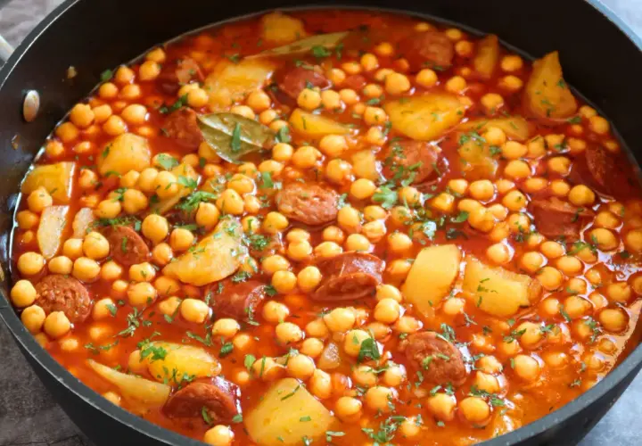 Un plato humeante de garbanzos con chorizo arguiñano, patatas y perejil picado en una sartén negra.
