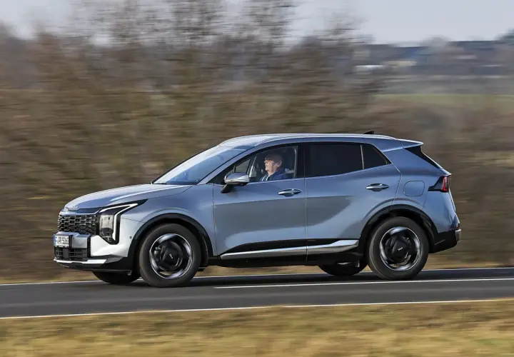 Srebrny SUV Kia Sportage, jeden z najnowszych modeli, jedzie po drodze.