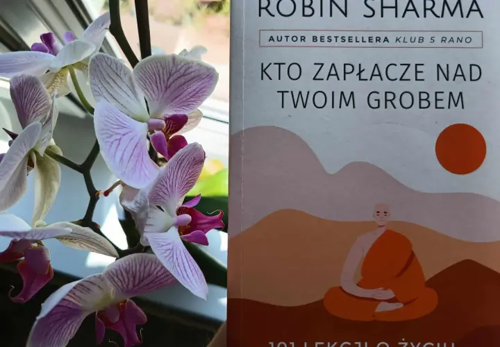 Delikatne storczyki obok książki "Kto zapłacze nad twoim grobem" Robina Sharmy, autora bestsellerów.